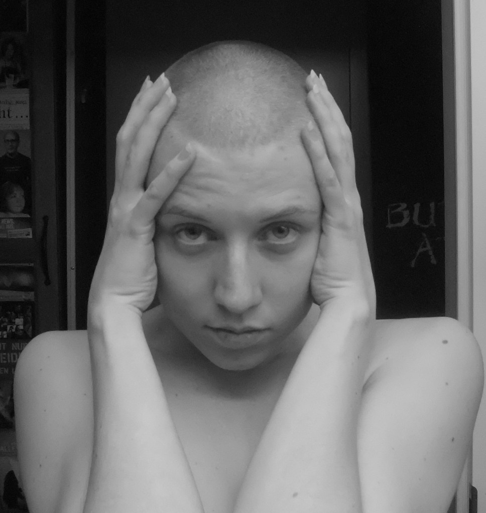 frau mit glatze, beide hände über den ohren, blick in die kamera