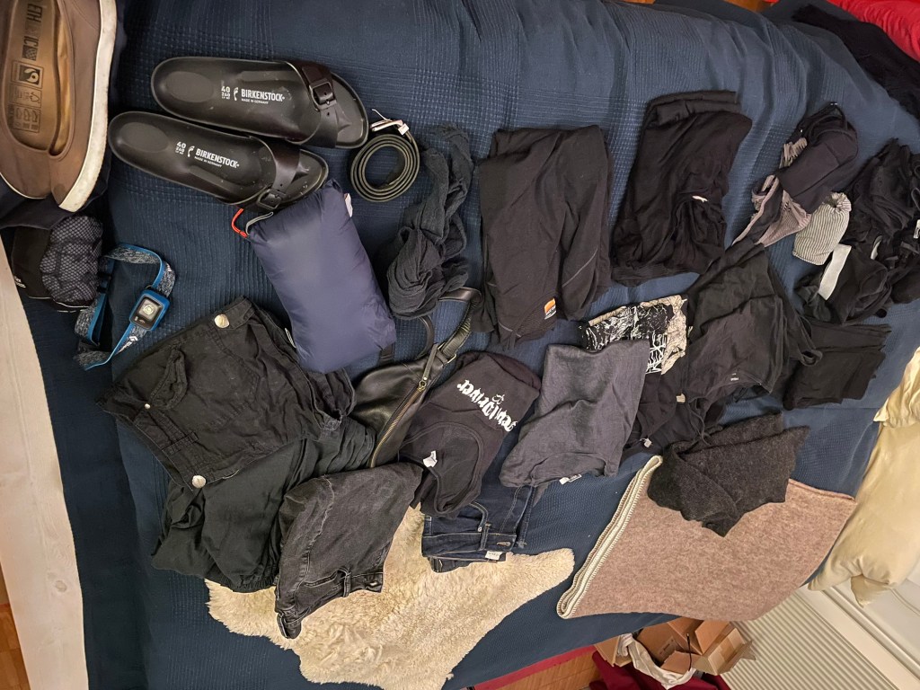 Stapel Kleidung in schwarz zeigt was ich für den Urlaub mitnehme