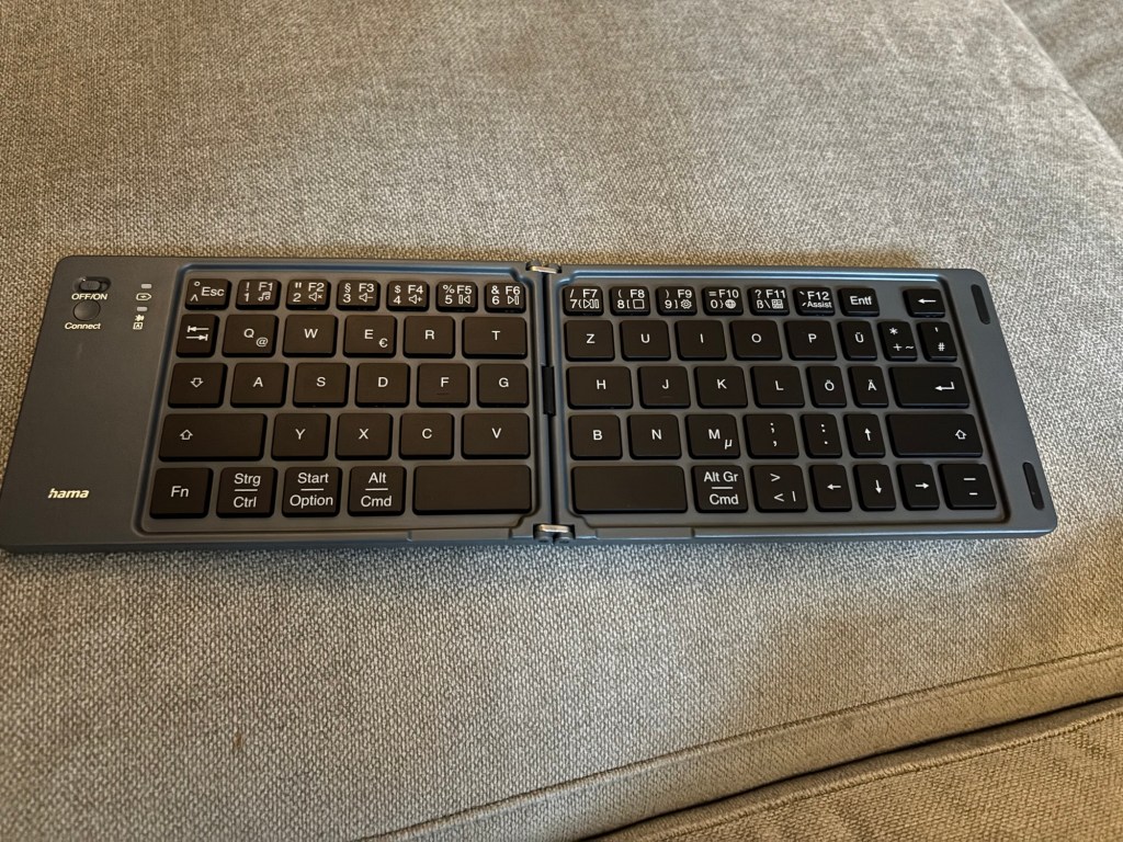 Bild der Tastatur im ausgeklappten Zustand. Zusammengeklappt ist sie ca. so groß wie mein Smartphone, ausgeklappt hat sie aber eine bequeme Breite, um mit zehn Fingern tippen zu können. Die Tasten, wie Sonderzeichen, sind allerdings teilweise anders angeordnet.
