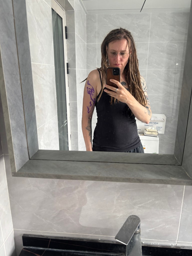 Selfie im Badezimmerspiegel mit dem Stenzel des Tattoomotivs auf dem linken Oberarm