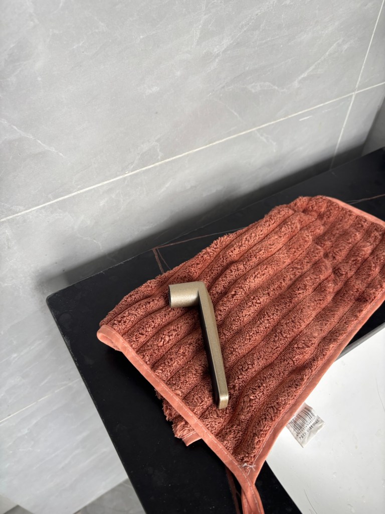 Neben einem Waschbecken liegt auf einem rotbraunen Handtuch eine Türklinke