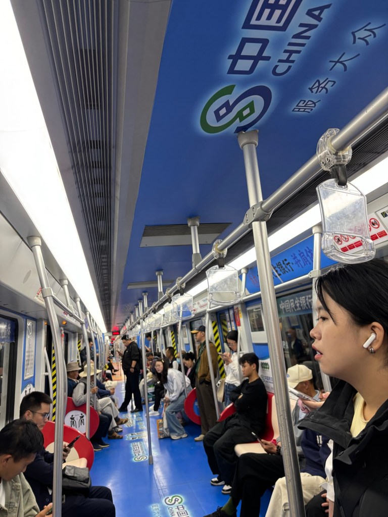 Menschen stehen und sitzen in einem U-Bahnwaggon. Der Waggon ist an den Wänden, auf dem Boden und an der Decke mit in Blautönen gehaltener Werbung beklebt.
