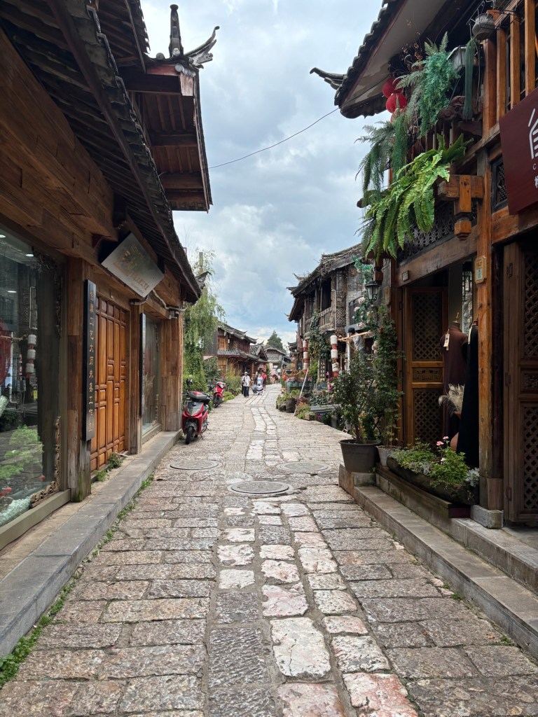 Gasse mit Kopfsteinpflaster, holzvertäfelten Fassaden und parkenden Rollern