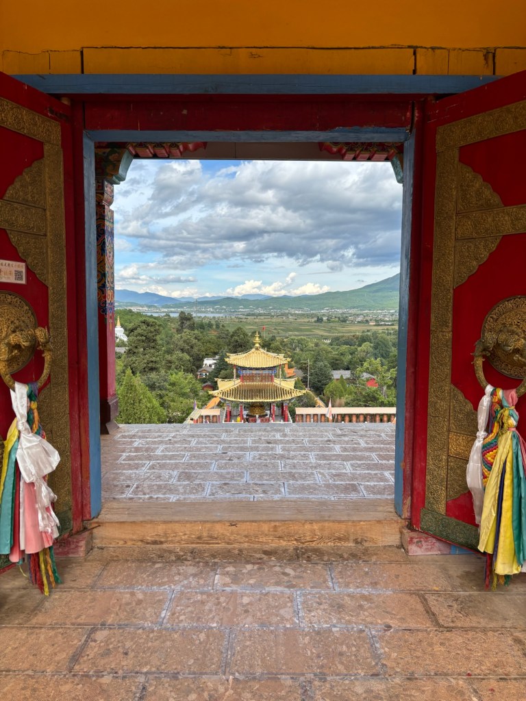 Blick durch eine Tür mit Troddeln auf ein weiter unter liegendes Gebäude mit goldenem Dach. Weiter hinten Bergkulisse
