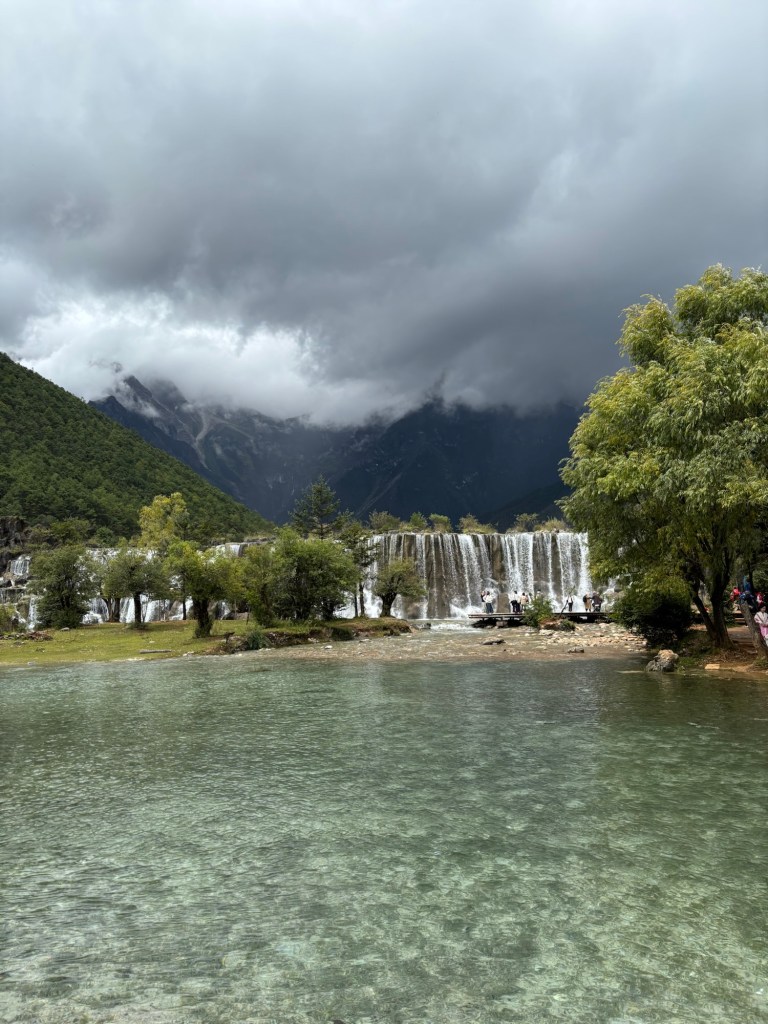 Ein breiter Wasserfall, im Hintergrund Berge und tief hängende Wolken