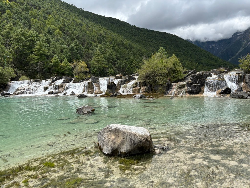 hellblaues Wasser, im Hintergrund ein Wasserfall über mehrere Stufen