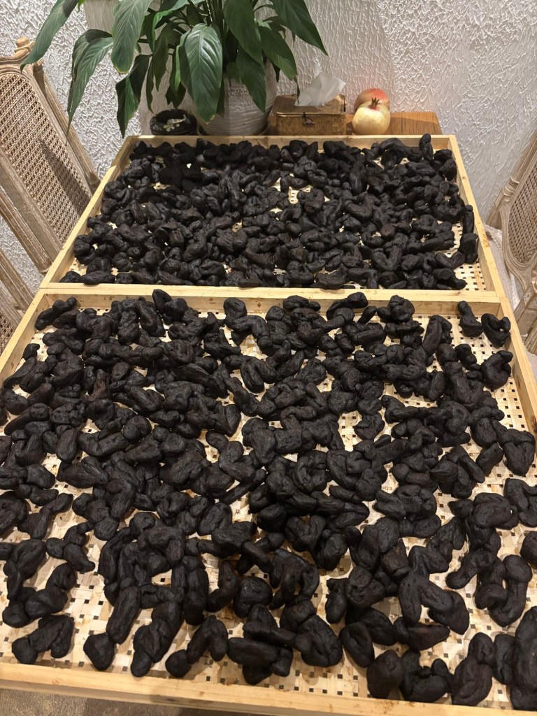 Zwei Holztabletts mit kleinen Löchern im Boden enthalten schwarz geräucherte Knollen sorgsam ausgebreitet