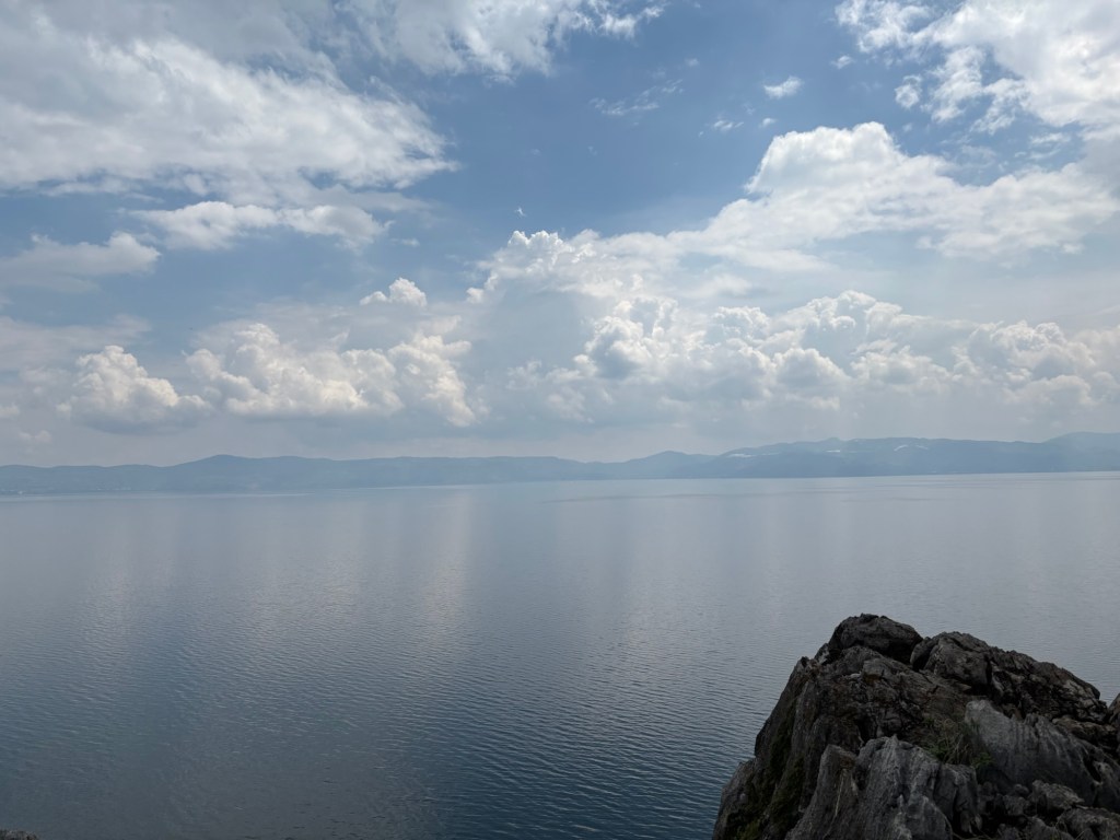 Die große Fläche des Fuxian Sees, das andere Ufer weit im Hintergrund mit sanften Hügeln, der Himmel ist locker weiß bewölkt
