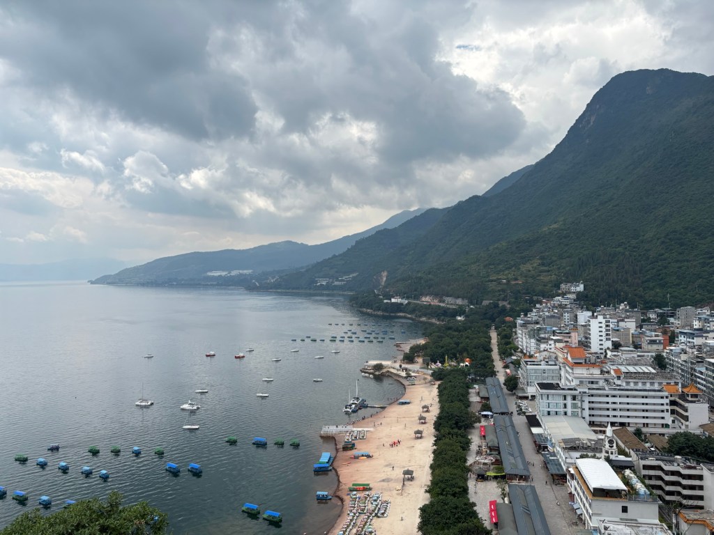 Das Ufer des Sees mit hellem Sand, ein Grünstreifen, dahinter kleinstädtische Bebauung